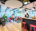 spacious office area, wooden flooring, red seating, modern decor, pendant lights, green plants, communal table with fruits