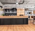 open reception desk, wooden reception top, black metal base, modern design, large monitor displays, potted plants, high ceiling with lights, wooden floor
