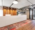 Modern and stylish office space with a large white reception desk, wooden accent walls, pendant lighting, and a patterned area rug on the hardwood floor. The space also features glass doors and windows, providing natural light and a view of the exterior.