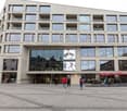 Multi-story commercial building with large windows, outdoor seating area, and advertisements displayed on the facade