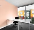Spacious office with large windows, white desk, black office chair, and colorful exterior building visible through the windows