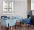 Spacious living room with large windows, light-colored furniture including sofas and armchairs, wooden flooring, and a minimalist design aesthetic.
