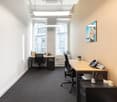 Spacious office with large windows, hardwood desk, office chairs, and a wall-mounted artwork. The room also features a phone and a small plant on the desk.