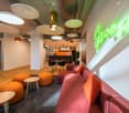 Modern and colorful office space with comfortable seating areas, large circular lighting fixtures, and a neon sign on the wall
