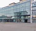A multi-story commercial building with a glass facade, housing various businesses such as Buche, Regus, and Binelli Group. The building has a parking lot in front and appears to be located in an urban area with a tram station nearby.