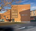 Large modern building with a brown facade, featuring the Regus and BPS (SUISSE) logos. The building has a distinctive architectural design with horizontal lines and windows. There are trees in the foreground, indicating an outdoor setting.