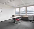 Spacious office room with large windows, white walls, suspended ceiling, desk, chairs, and storage cabinets