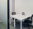 Glass partition, white desk, two black swivel chairs, picture frame with a plant, writing utensils