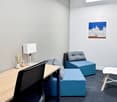 a desk with a chair, a desk lamp, two modular sofa seats, a potted plant, and a painting on the wall