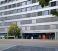Multistory building with multiple windows, modern architecture, large entrance with 'conex' signage, streetlight, trees, empty street, aldi store.