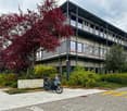 4-story building, glass windows, metal balconies, parking spot, trees, bushes