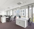 Empty office with desks and office chairs facing the window, carpet flooring, glass walls, white cabinets