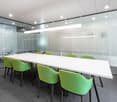 long white table, green chairs, glass walls, gray carpet, fluorescent ceiling lights