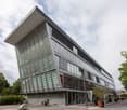 modern office building, glass facade, multiple floors, angled roof, large windows, outdoor area with plants and trees