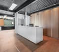 Reception area with white desk, wooden floor, wooden wall, monitors, lamps, and a window