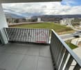 Balcony with a view of a grassy field, surrounded by apartment buildings and mountains in the background