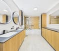 Spacious bathroom with wood-paneled walls, double vanity sinks, large round mirrors, and a glass-enclosed shower area