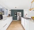 Modern kitchen, white countertops, wooden floor, green cabinets, stainless steel appliances, large window