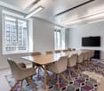 Long wooden table with wooden chairs, flat screen TV on wall, large windows, carpets