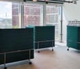 Large open office space with floor-to-ceiling windows, mobile partitions in green color, and a sign that says 'For new business opportunities, it helps being around'