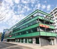 Modern building, multiple floors, green facade, office sign 'SPACES', large glass windows, road in front