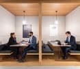 Private meeting booth with two desks, wooden partition walls, and tables, with two people working or conversing.