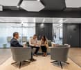 Modern and stylish office space with comfortable seating, glass walls, and geometric patterns on the walls. Three people are seated in the lounge area, engaged in a discussion.