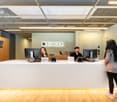 Open office space with reception desk, computers, and employees working at desks. The space has a modern, minimalist design with wooden accents and a large 'SPACES' logo on the wall.