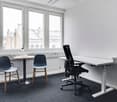 Empty room with large windows, two chairs, a small table, an office chair, and a desk with an adjustable height feature