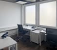 modern office with white walls, wooden floor, desks, chairs, windows, telephones, and a ceiling light