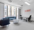 modern office, large windows, minimalist design, two blue couches, white desk, two black office chairs, grey carpet, artwork on wall
