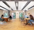 modern office space with wooden floor, large windows, round table, chairs, lamps, wall clocks, and a long bench