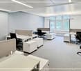 modern office space with white desks, black chairs, gray walls, white ceiling, large windows, white cabinets, and white flooring