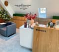 Interior of office space, features a desk, couch, small plants, decorative items, a whiteboard, wooden furniture, a window with a view of a house, and a quote on the wall.