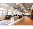 Large office reception area with a reception desk, two employees at desks, large windows, wooden floors
