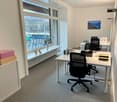 modern office with white walls, white desks, black office chairs, large window with balcony, radiator, storage boxes, plants