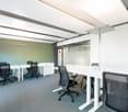 modern office with white desks, black chairs, carpeted floor, glass walls, ceiling lights