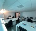 Empty office room with white tables and chairs, monitors, and a standing lamp.