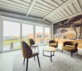 Modern room with beige furniture, wooden table, large windows, wooden walls, carpet, large artwork