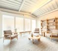 spacious living area, large windows, modern furniture, bookshelves, carpet, lamps, wooden coffee table, white ceramic vases, cushions, books