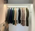 A room with a wall-mounted rack holding various coats. The wall is painted white, and there's a lit LED strip running along the ceiling of the rack. Below the rack, there is a wooden floor.
