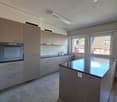 modern kitchen with island, gas oven, ceramic counter top, 2 windows, grey kitchen cabinets, power outlets, extractor fan, sink with faucet, large kitchen island