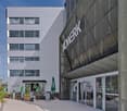 Multi-story commercial building with a large sign that says 'KONECRANES'. The building has glass windows and a patio area with outdoor seating. There is a parking area in front of the building.