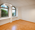 large room, wooden parquet flooring, white walls, circular lamps, arched windows with white frames, window sills