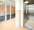 Elevator access to an entrance with sliding glass doors, tiled flooring and walls, a wall with a mailbox and a lift.