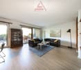 Spacious living room with hardwood flooring, large windows, a wooden cabinet, two leather sofas, a coffee table, and a floor lamp. The room has access to a balcony or terrace.