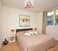 Spacious bedroom with large windows, hardwood floors, a king-size bed, bedside tables, and a decorative painting on the wall.
