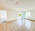 Spacious room with tile flooring, white walls, and large windows providing natural light. The room appears to be an open living or dining area.