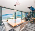 Spacious living area with large windows offering a scenic view of the mountains, wooden dining table, modern furniture, and a staircase leading to an upper level.
