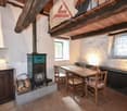 A fireplace and a dining table with chairs, a wooden cabinet, and wooden beams on the ceiling